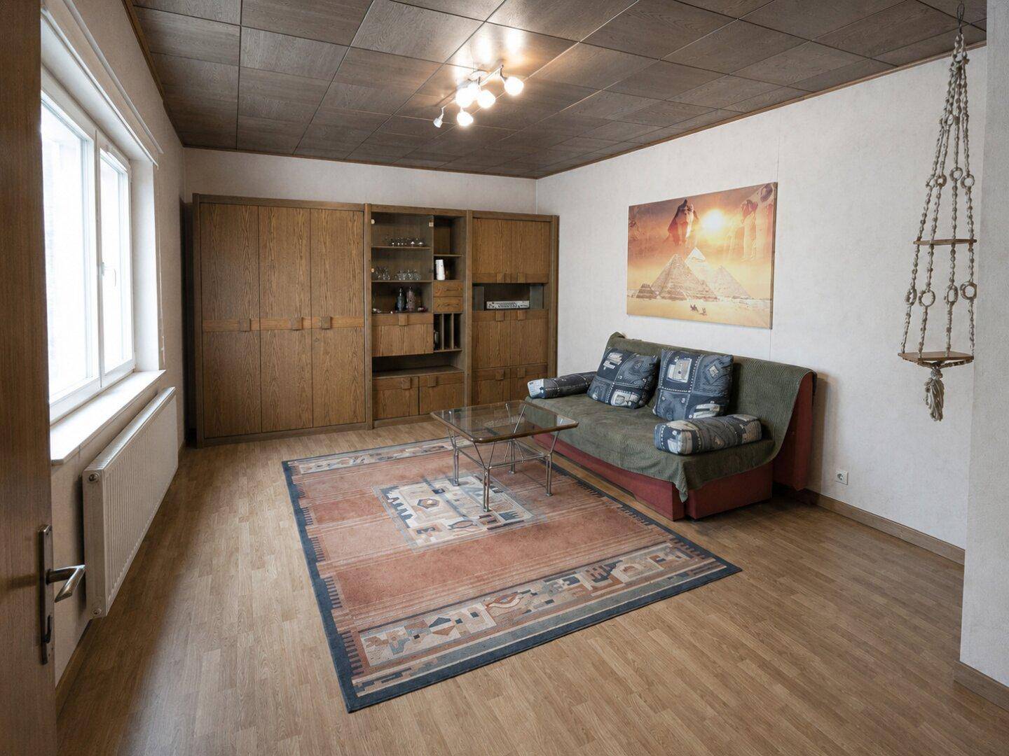 Wohnzimmer mit Sofa, großem Holzschrank und Teppich auf Parkettboden.