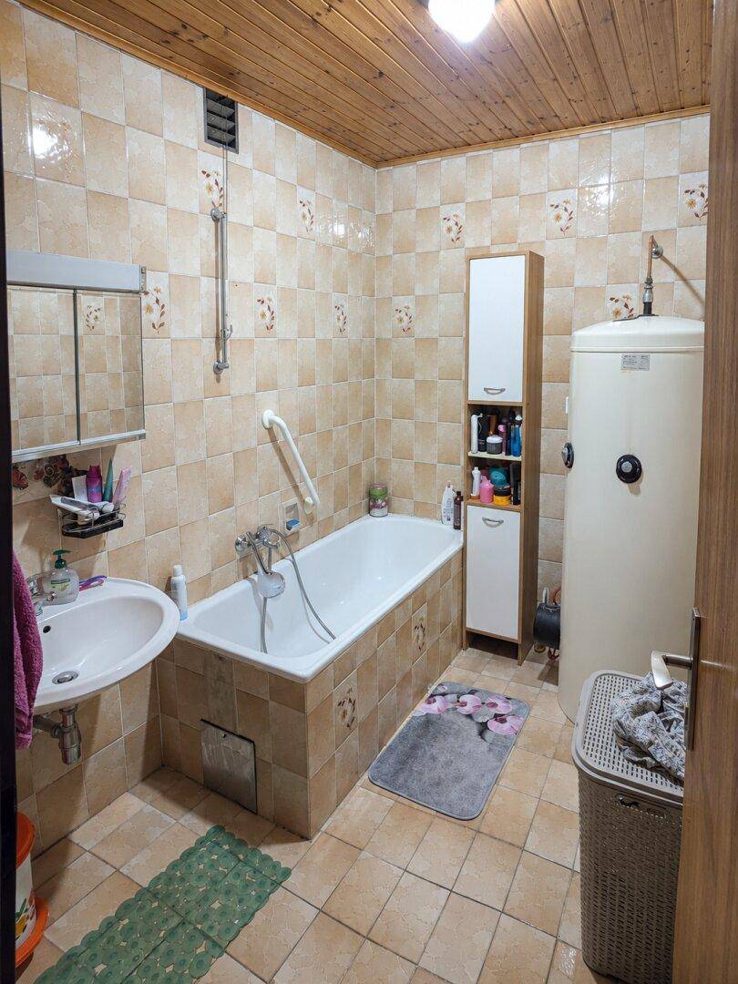 Badezimmer mit Badewanne, Waschbecken und Warmwasserboiler, geflieste Wände.