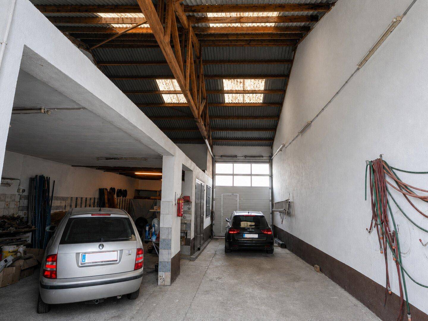 Geräumige Garage mit zwei geparkten Autos und hoher Decke mit Holzbalken.
