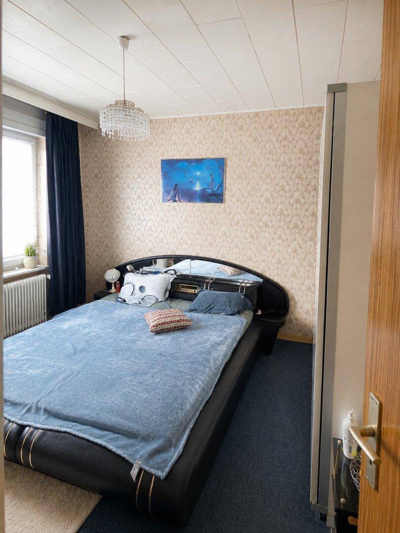 Schlafzimmer mit Doppelbett, gemusterter Tapete und Kronleuchter.