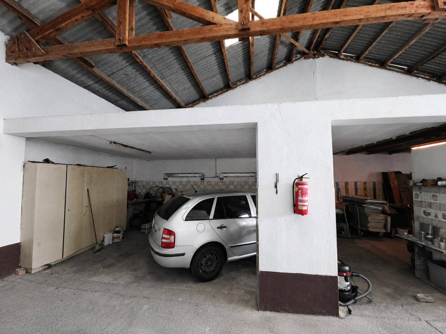 Geräumige Garage mit geparktem Auto, Lagerbereich und sichtbaren Holzbalken.