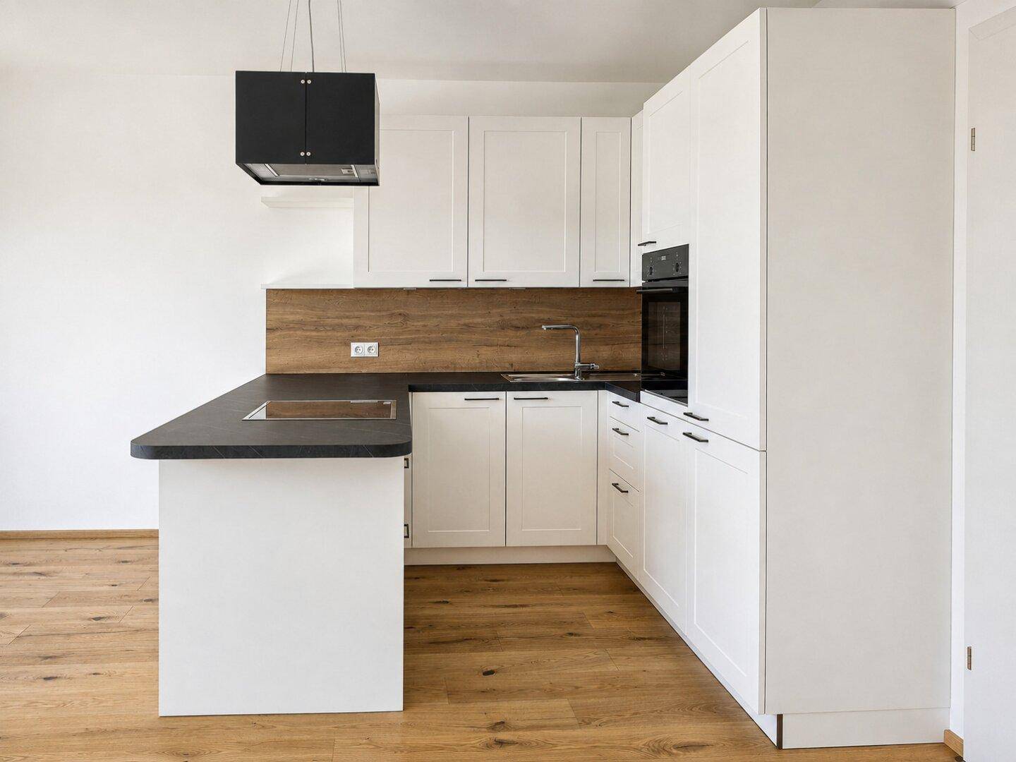 Moderne Einbauküche mit weißen Schränken, dunkler Arbeitsplatte und integrierten Geräten.