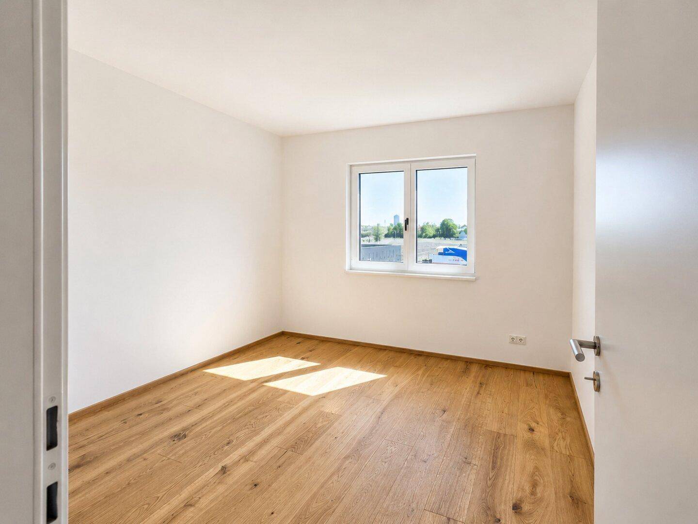 Freundliches Zimmer mit Holzboden und großem Fenster, ideal als Kinder- oder Arbeitszimmer.