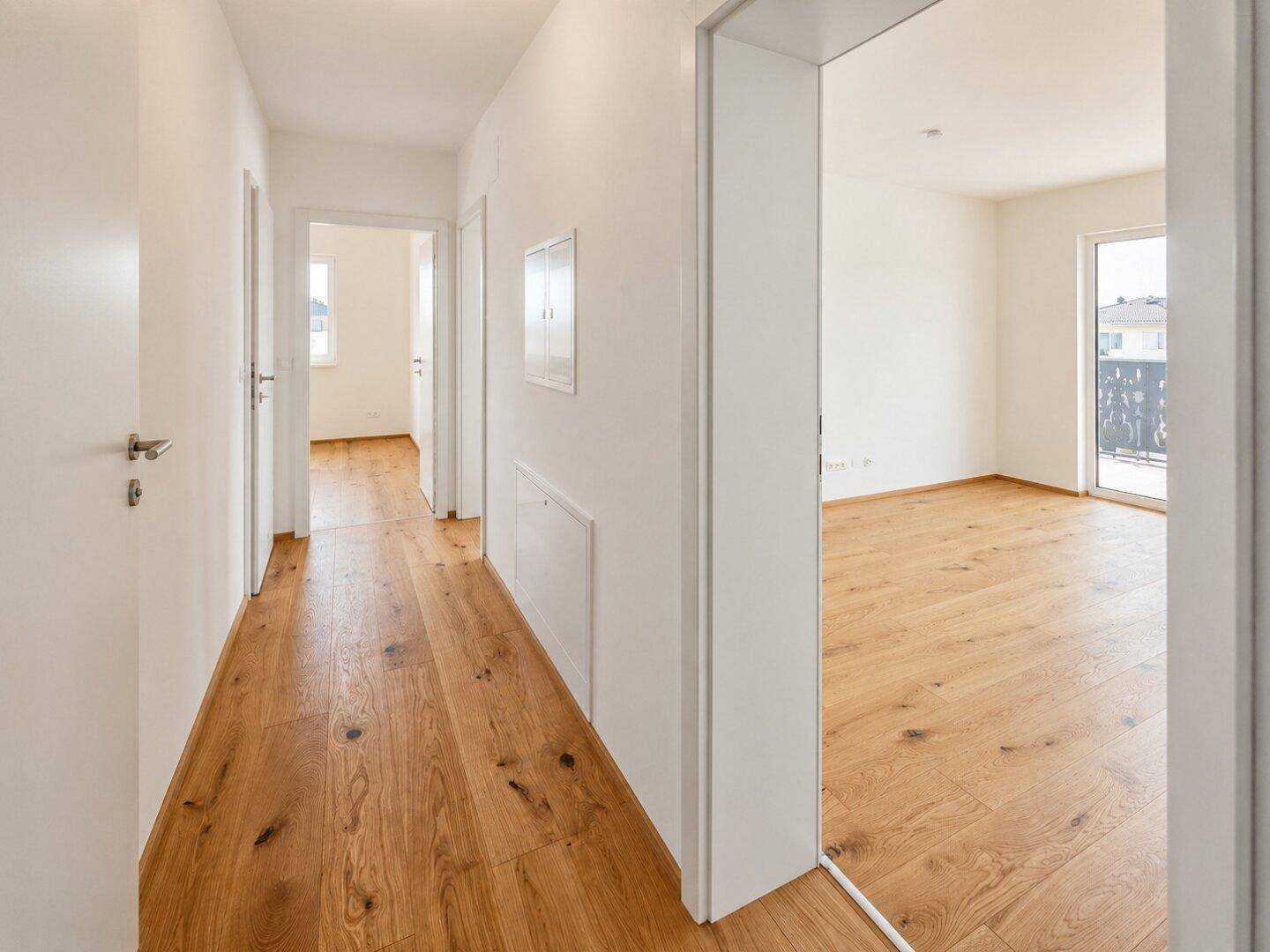 Heller Flur mit Holzboden, der zu verschiedenen Zimmern der Wohnung führt.