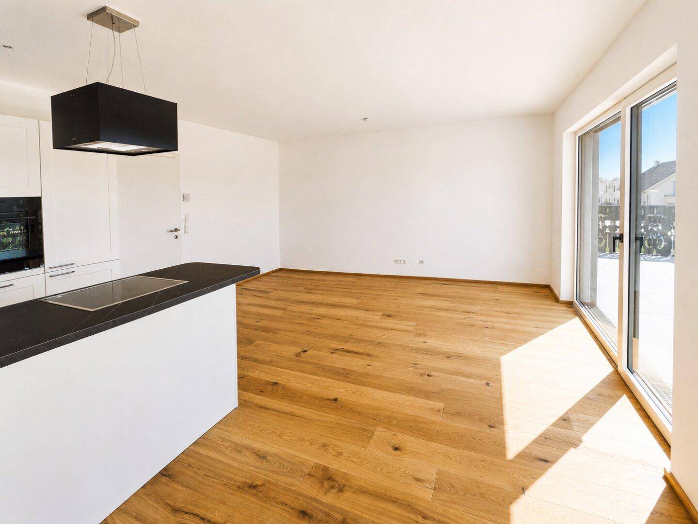 Geräumiger Wohnbereich mit offener Küche, Holzboden und viel Tageslicht.