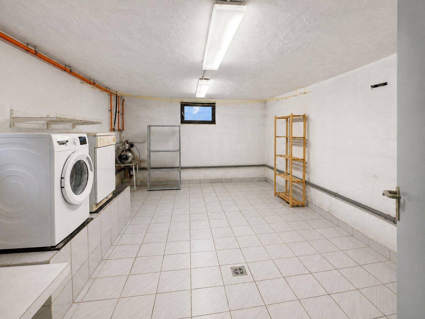 Praktischer Hauswirtschaftsraum im Keller mit Waschmaschine, Trockner und Fliesenboden.