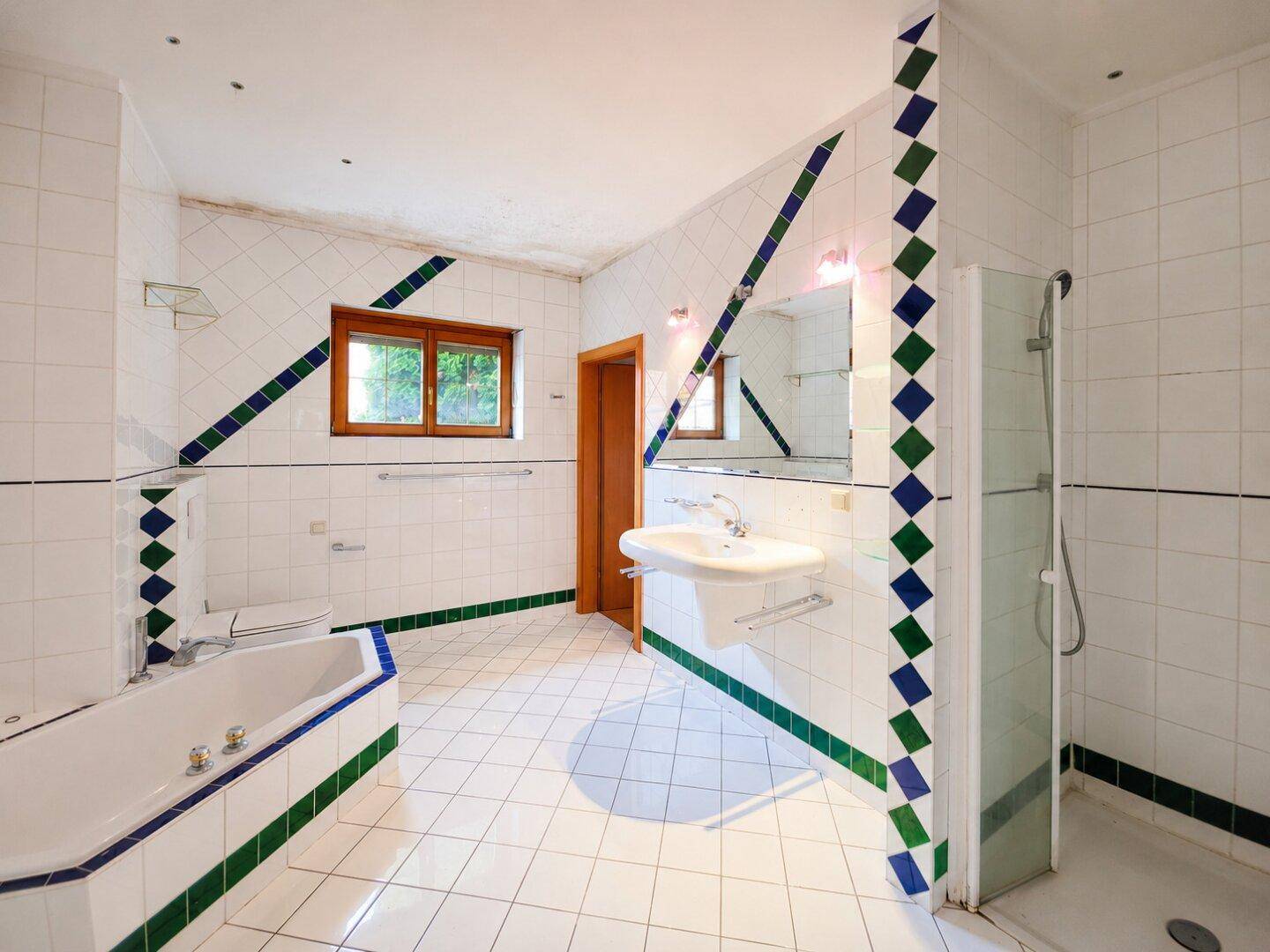 Geräumiges Badezimmer mit weißen Fliesen, farbigen Akzenten, Badewanne, Dusche und Fenster.