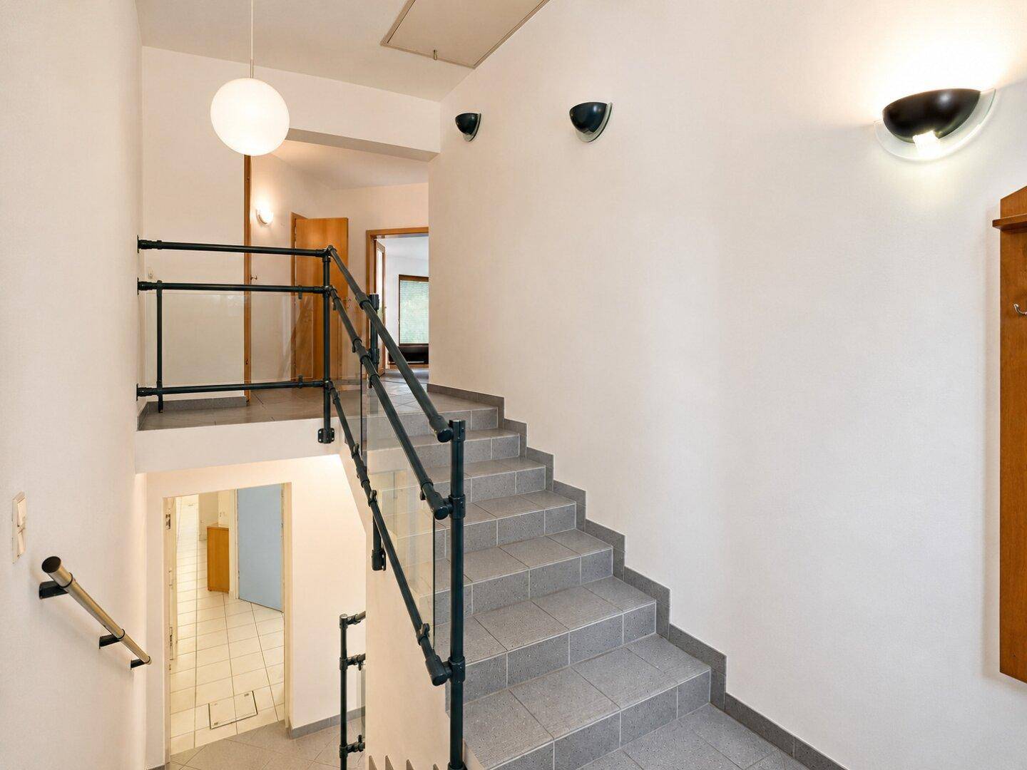 Treppenhaus mit grauen Fliesenstufen und modernem Metallgeländer, das die Etagen verbindet.