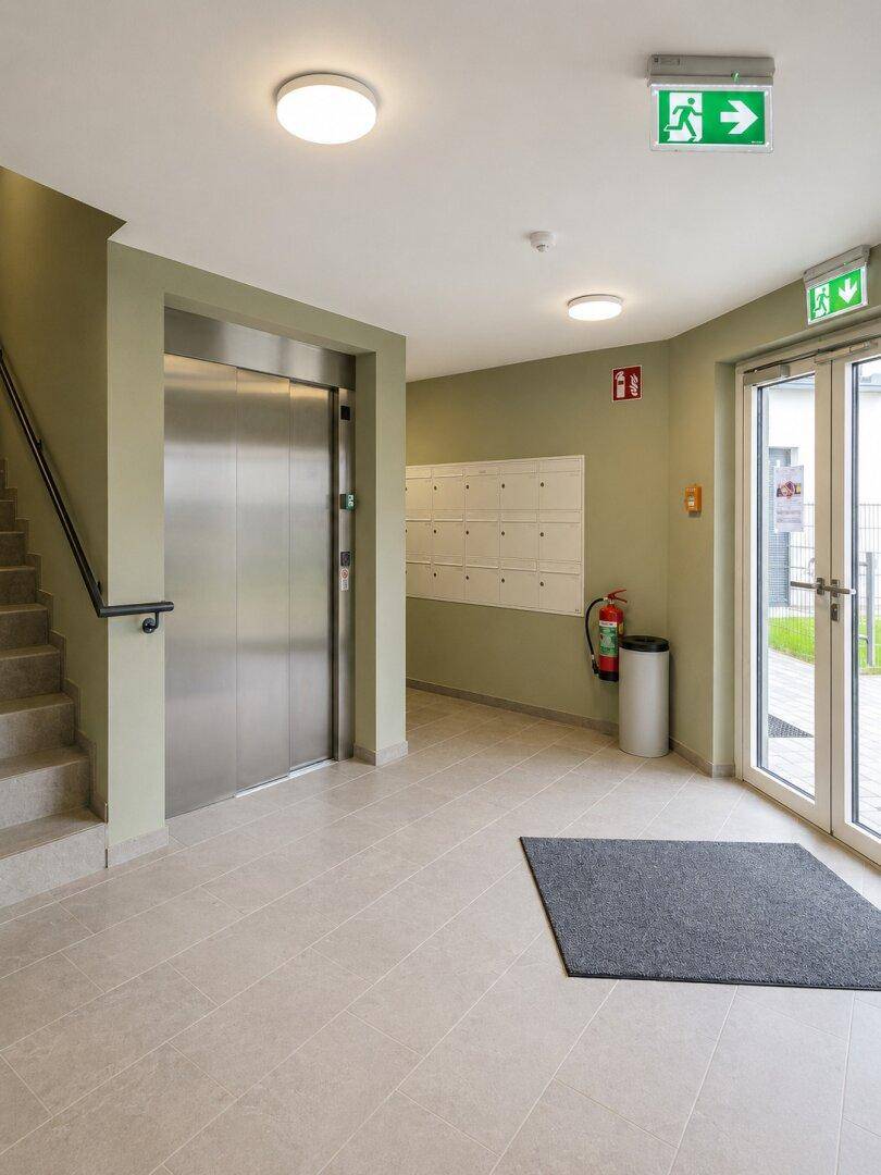 Heller Eingangsbereich eines Mehrfamilienhauses mit Aufzug, Treppe und Briefkästen.