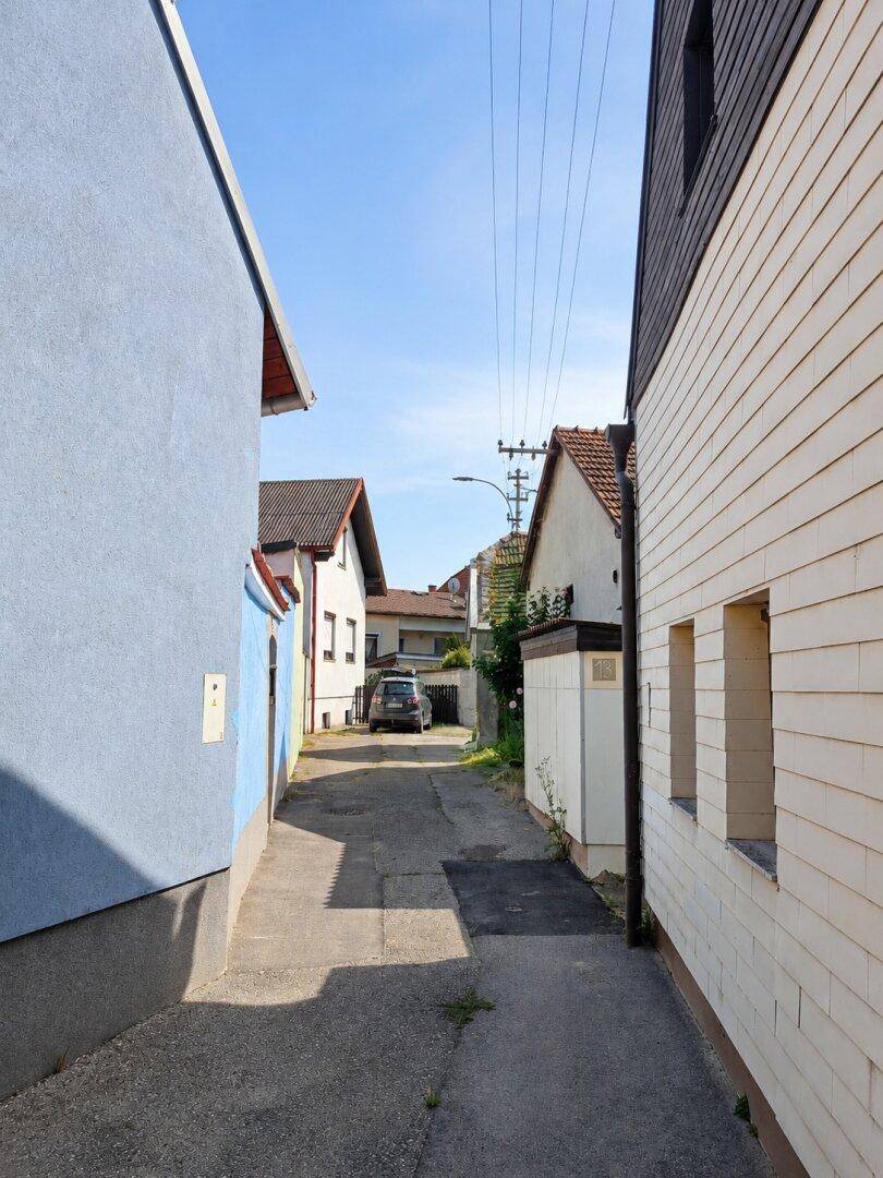 Schmale Gasse zwischen Gebäuden mit Blick auf die Nachbarschaft und ein geparktes Auto.