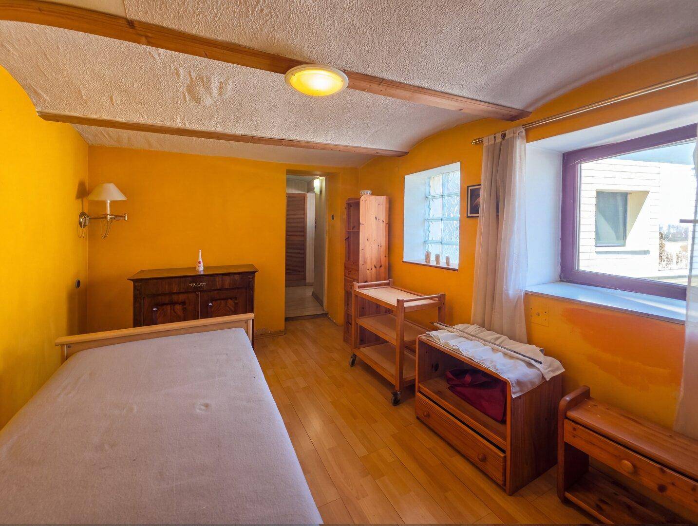 Helles Schlafzimmer mit gelben Wänden, Holzboden und Fenster mit Blick nach draußen.