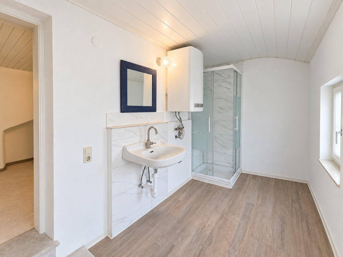 Modernisiertes Badezimmer mit Duschkabine, Waschbecken und Holzdeckenverkleidung.