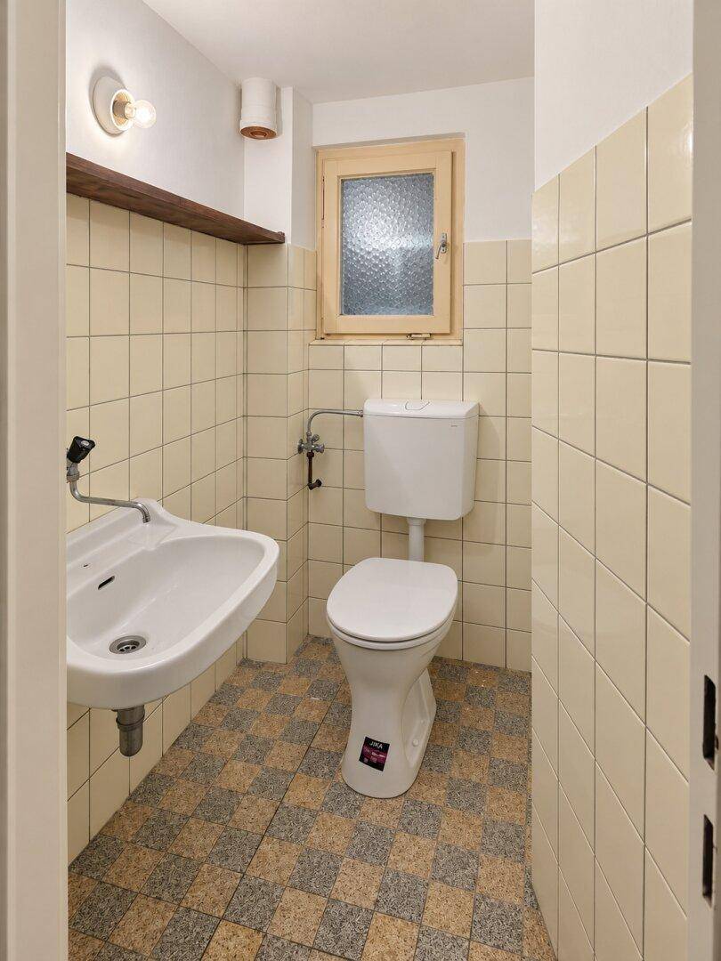 Kleines WC mit Toilette, Waschbecken und Fenster, komplett gefliest.