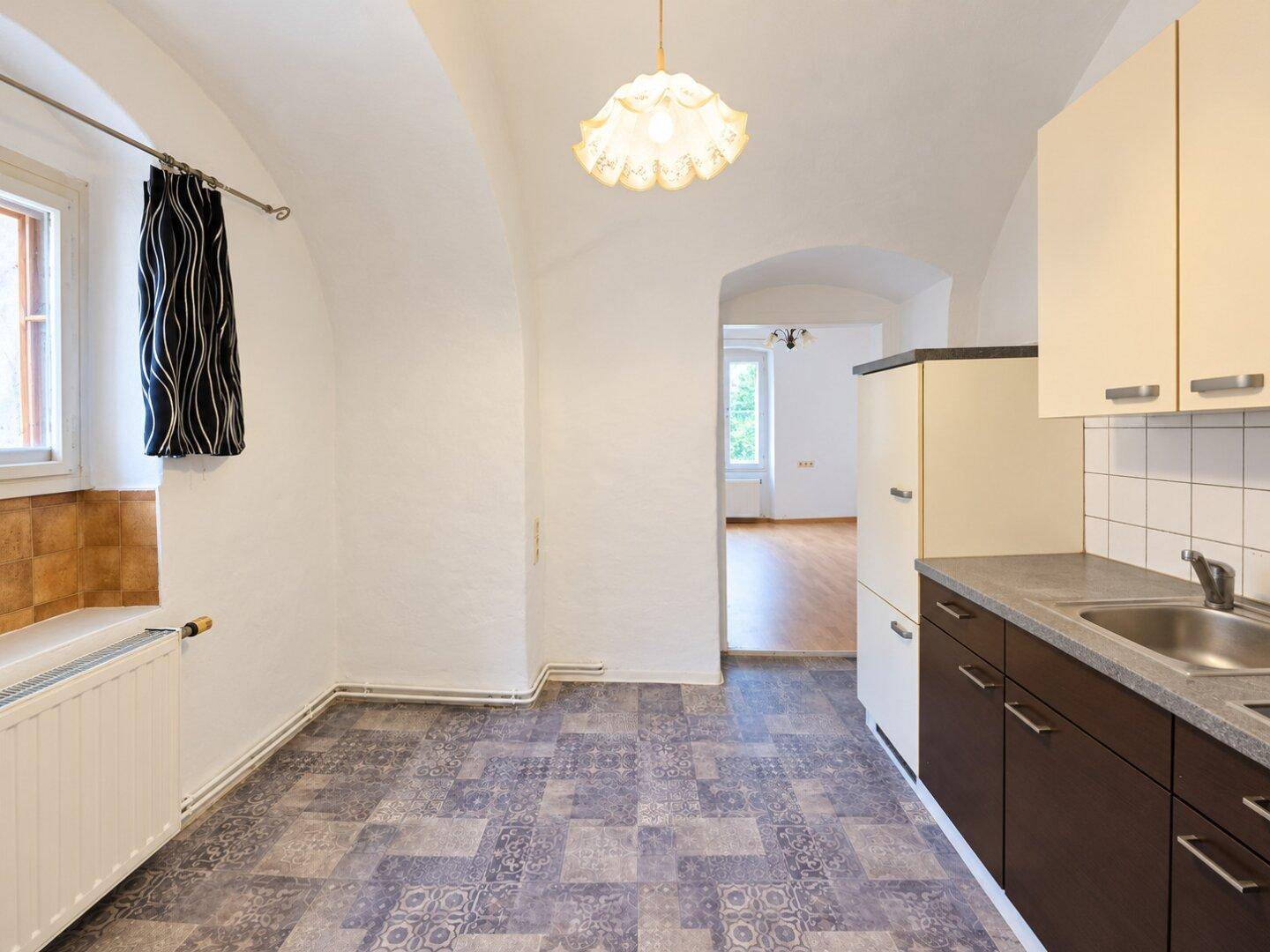 Küchenzeile mit Spüle und Blick durch einen Bogen in einen weiteren Raum mit Holzboden.