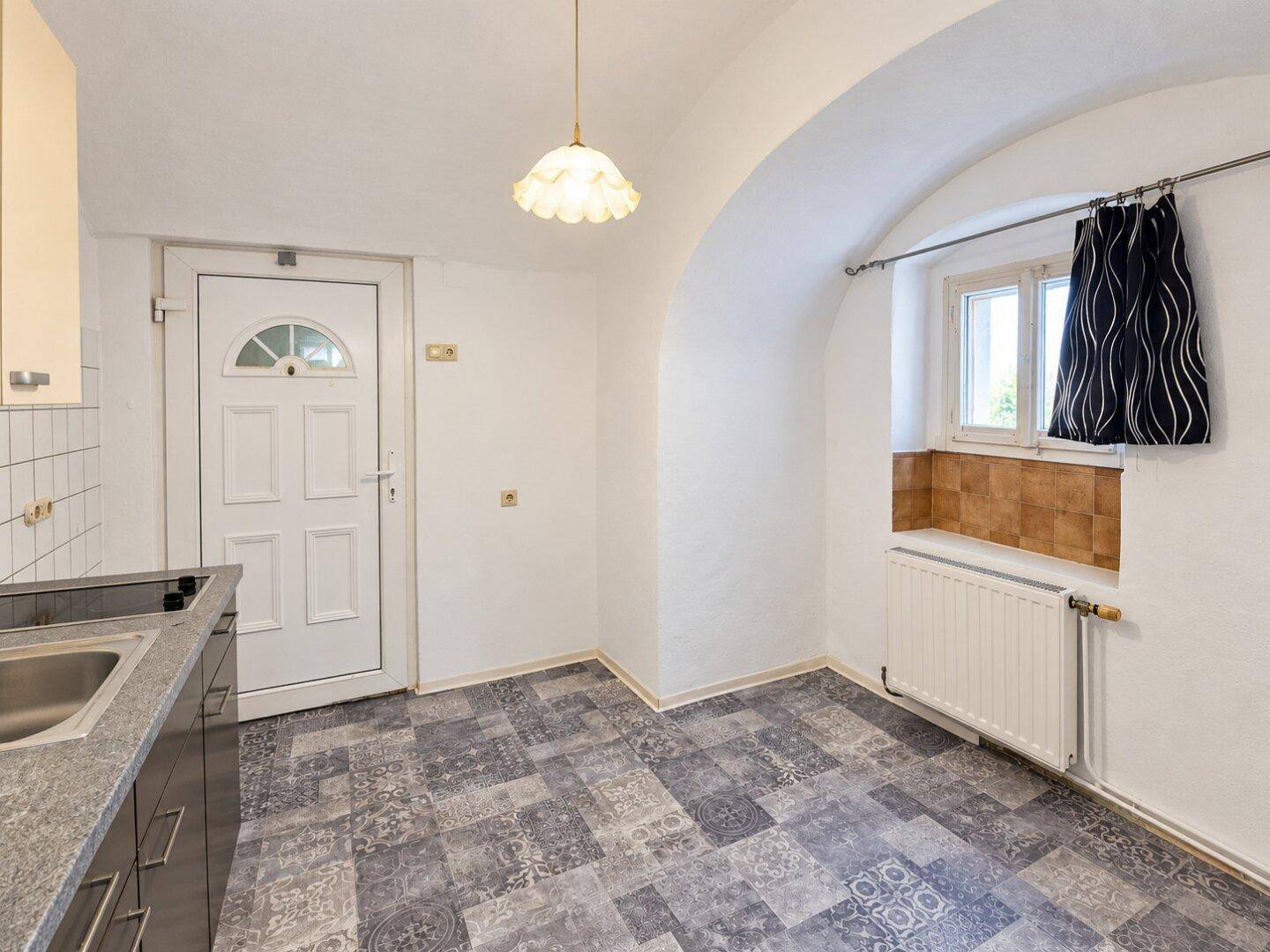 Küchenbereich mit Fenster, Heizung und gemustertem Bodenbelag in einem Raum mit Gewölbedecke.