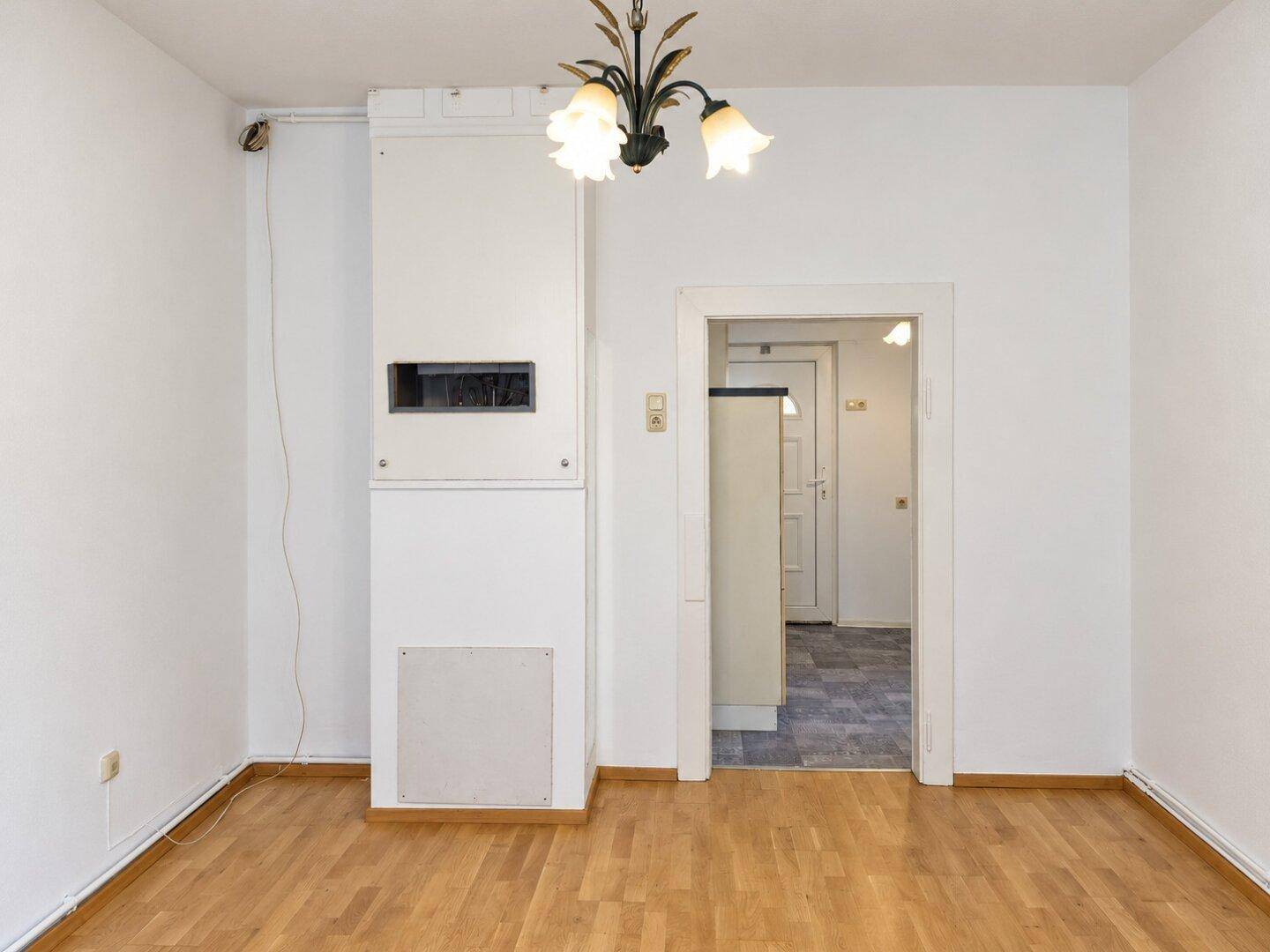Leeres Zimmer mit Parkettboden und Zugang zu einem weiteren Raum mit Fliesenboden.