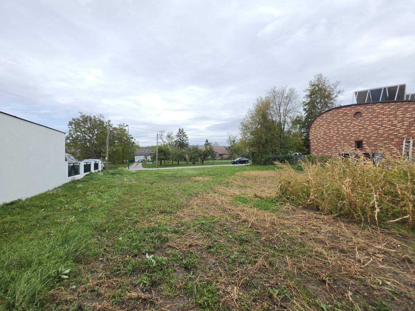 Grundstück mit spärlichem Gras, umgeben von modernen und traditionellen Gebäuden unter bewölktem Himmel.