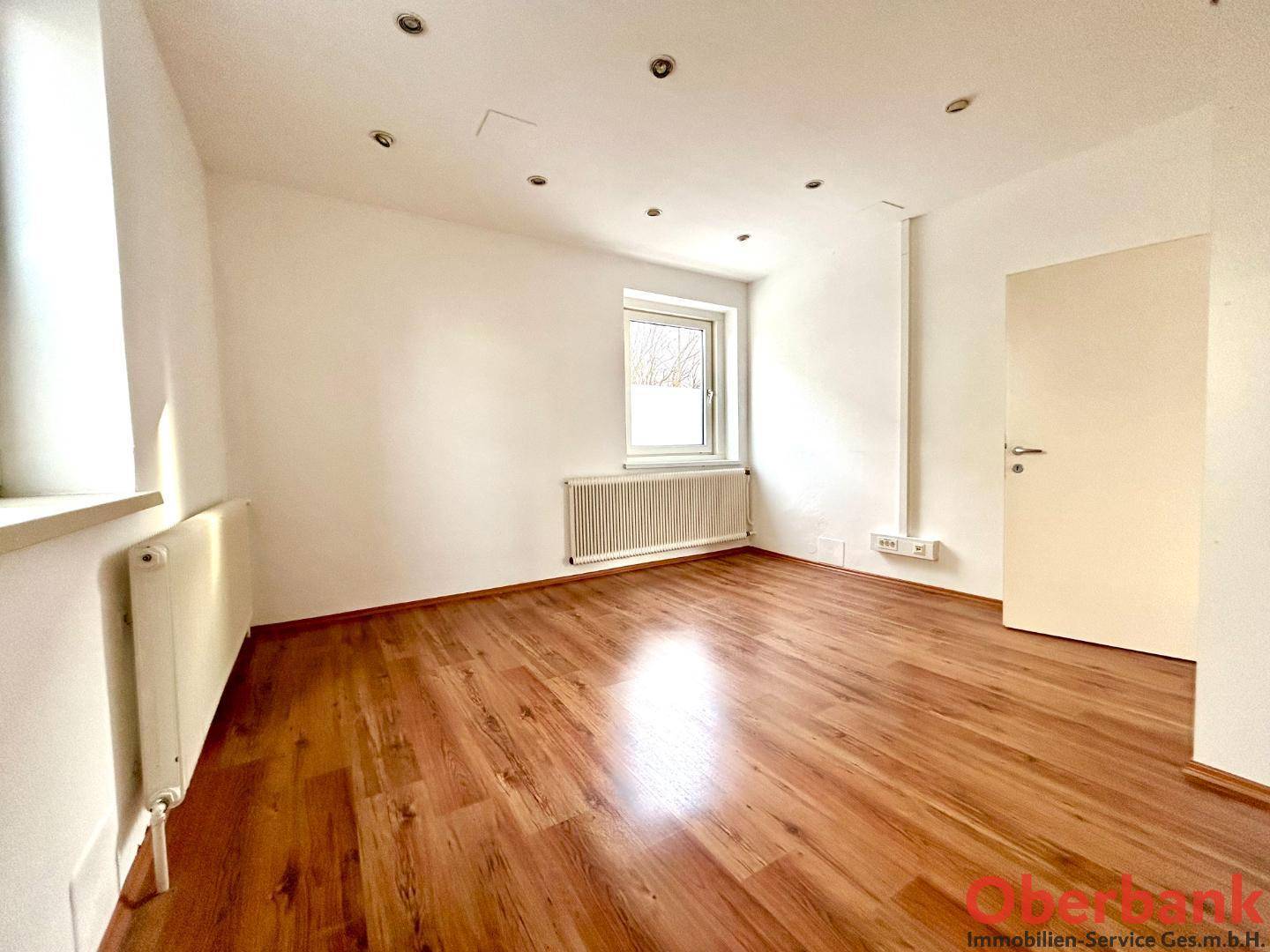 Kleineres Büro mit Laminatboden, einem Fenster und weißen Wänden, ideal für Einzelarbeitsplätze oder Besprechungen.