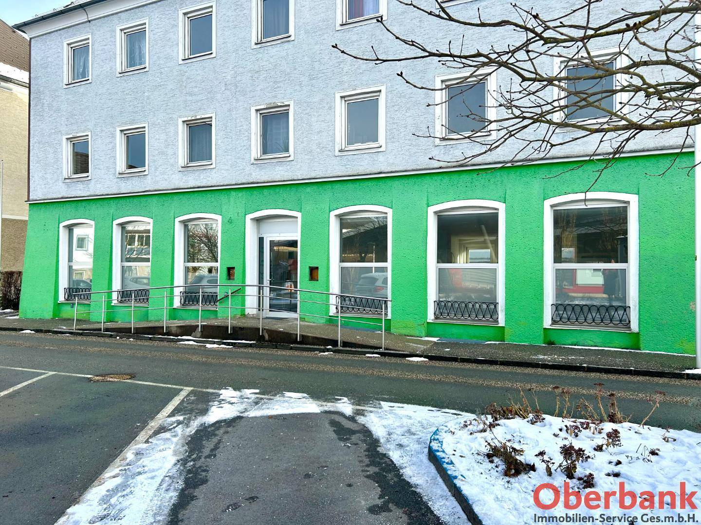 Außenansicht eines Geschäftsgebäudes mit auffälliger grüner Fassade, großen Schaufenstern und einer Rampe.