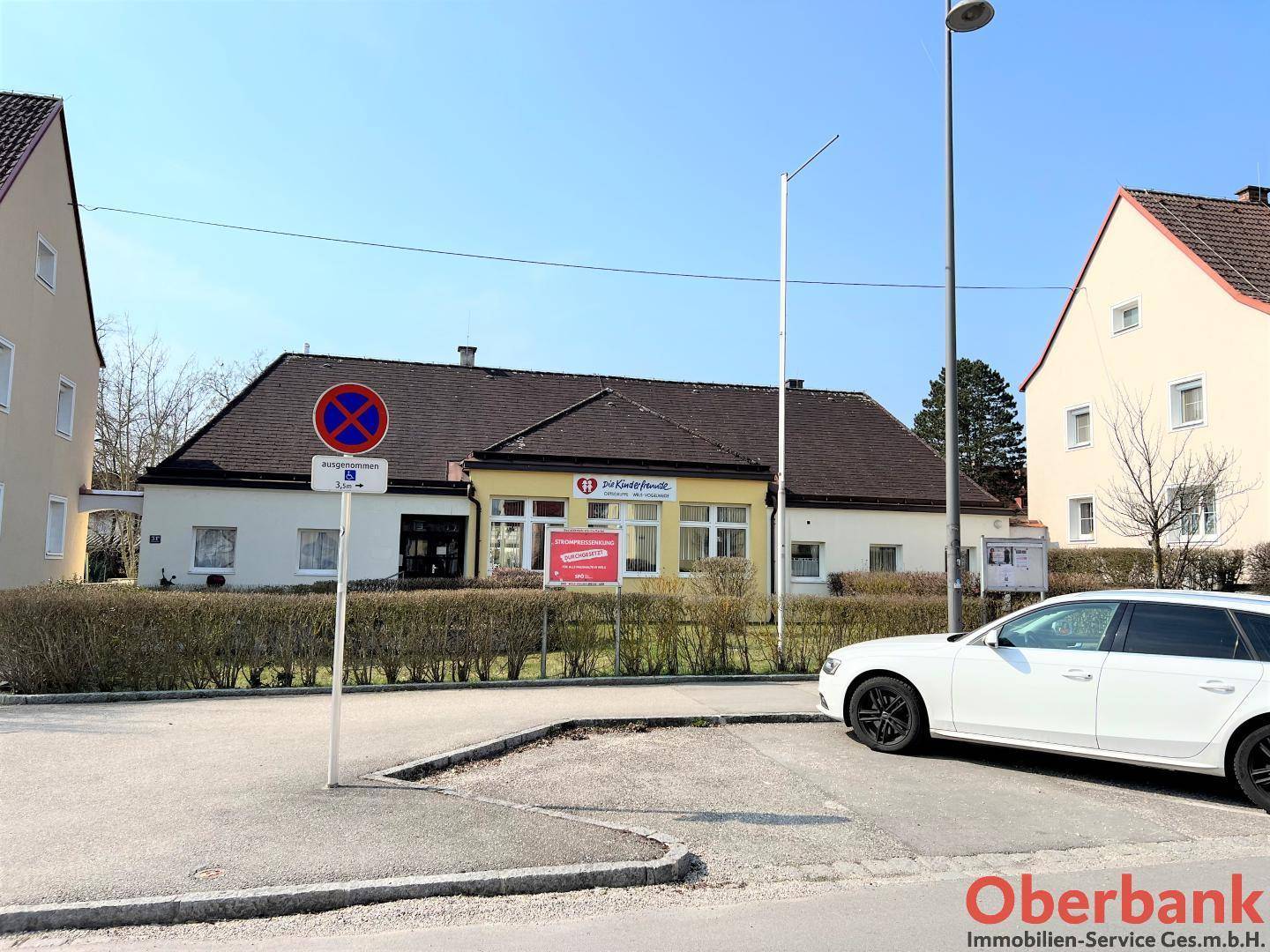 Außenansicht des Gebäudes von der Straße aus mit einem geparkten Auto und Schildern.