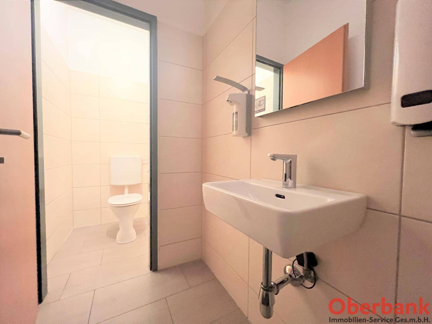 Modernes WC mit Waschbecken, Spiegel und hellen Fliesen an Wänden und Boden.