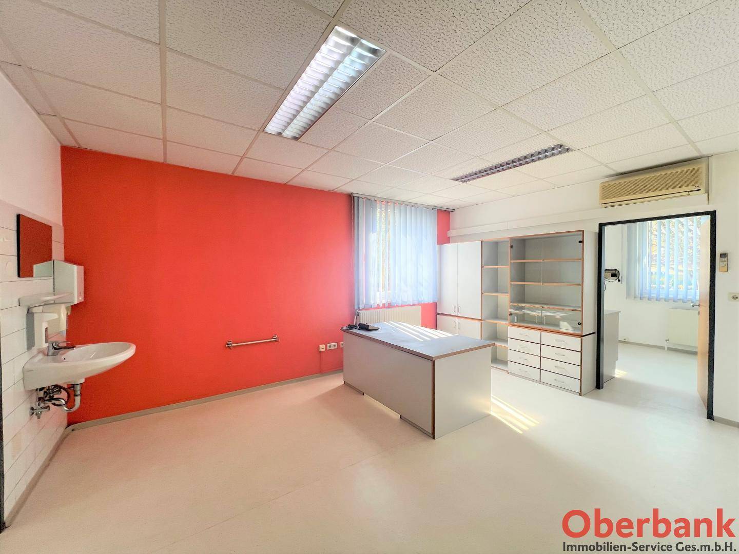 Büroraum mit einer auffälligen roten Wand, Waschbecken und Klimaanlage an der Decke.