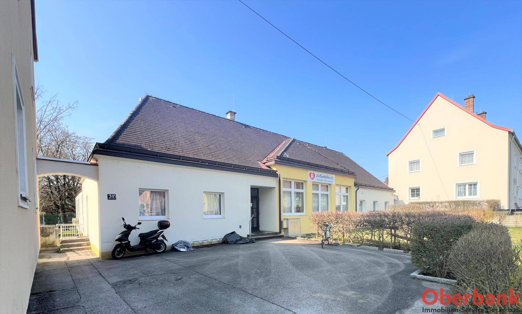 Außenansicht eines eingeschossigen Gebäudes mit Parkplatz und gepflegter Hecke.