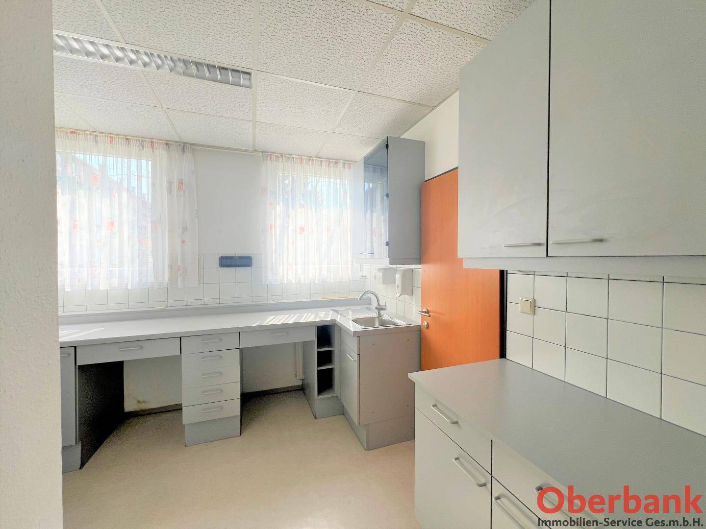 Funktionaler Laborraum mit weißen Fliesen, Arbeitsflächen und Spülbecken unter dem Fenster.