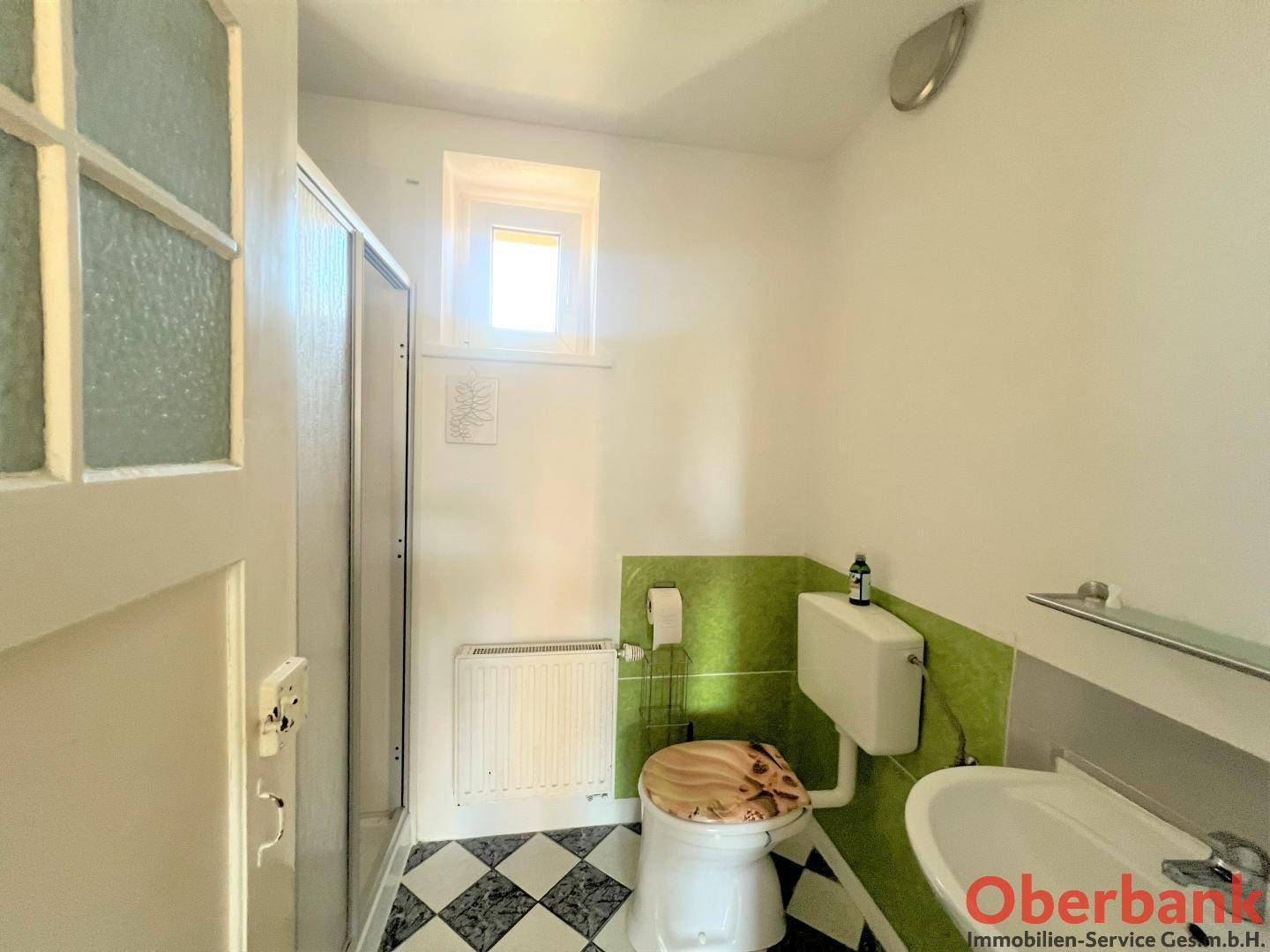Kleines Badezimmer mit Toilette, Waschbecken, Duschkabine und grün-weiß gefliesten Wänden.