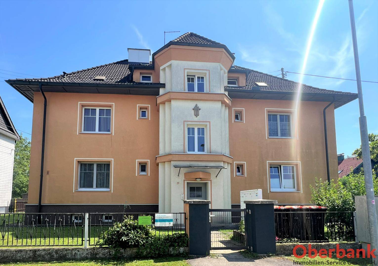 Vorderansicht eines Mehrfamilienhauses mit oranger Fassade, dunklem Dach und einem markanten Erker.