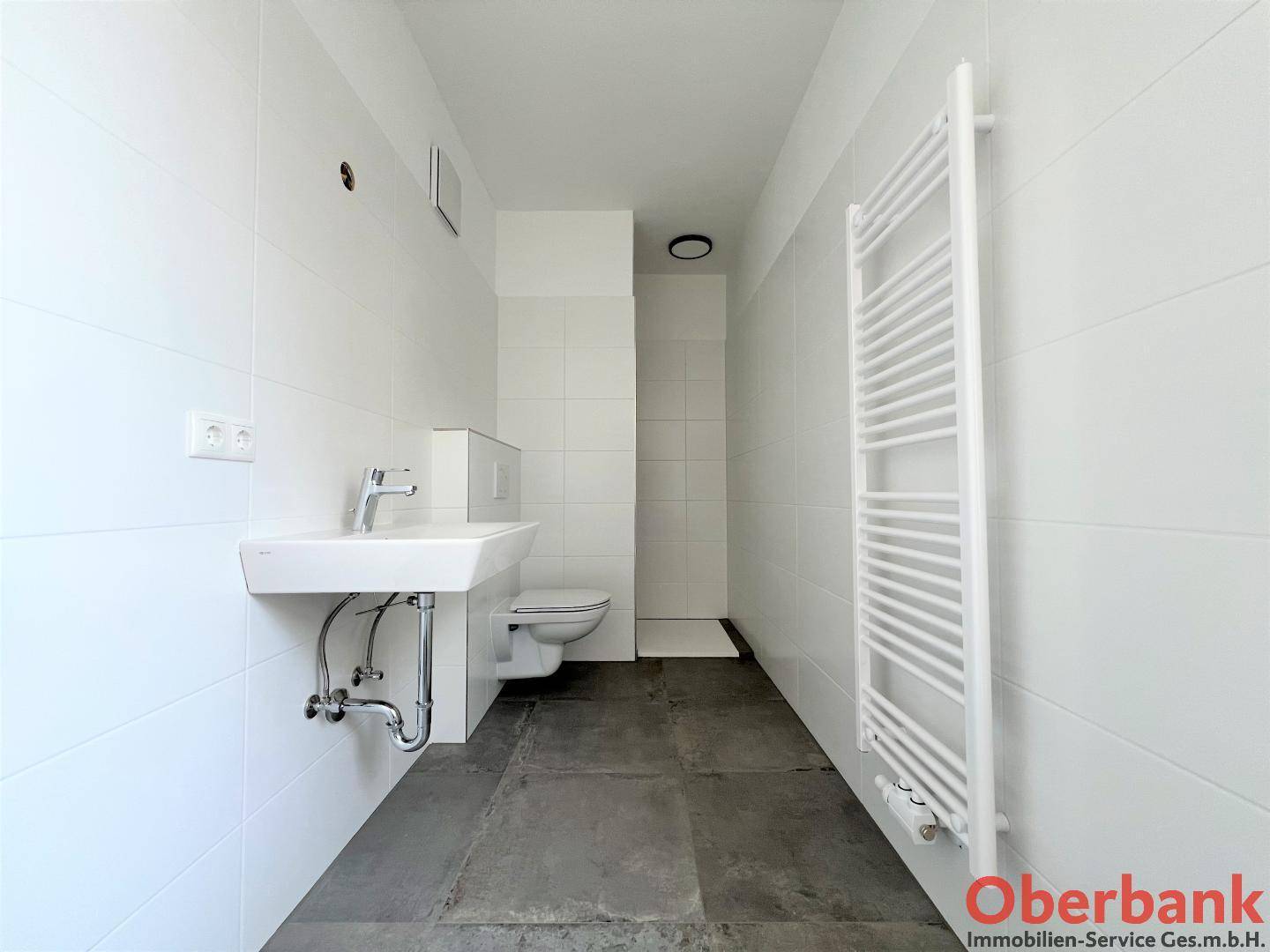 Modernes Badezimmer mit ebenerdiger Dusche, Wand-WC, Waschbecken und Handtuchheizkörper.