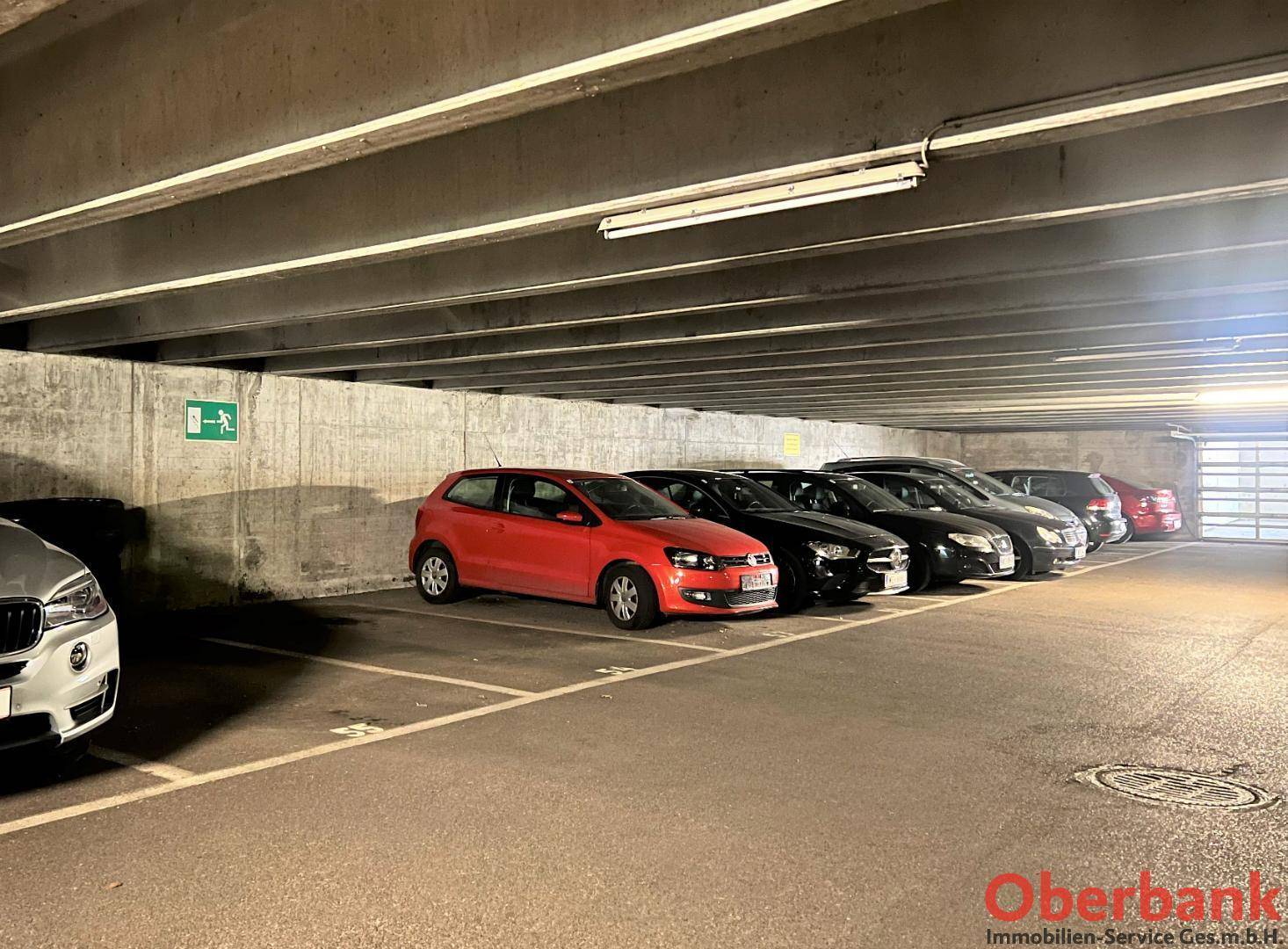 Tiefgarage mit mehreren geparkten Autos und Betonwänden unter künstlicher Beleuchtung.