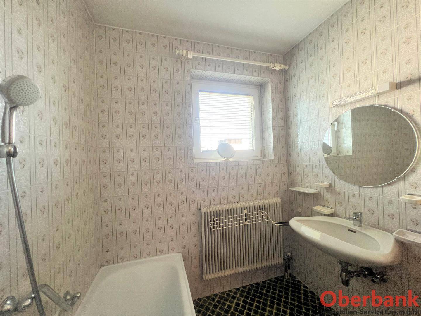 Badezimmer mit Badewanne, Waschbecken, Fenster und hellen, gemusterten Fliesen.