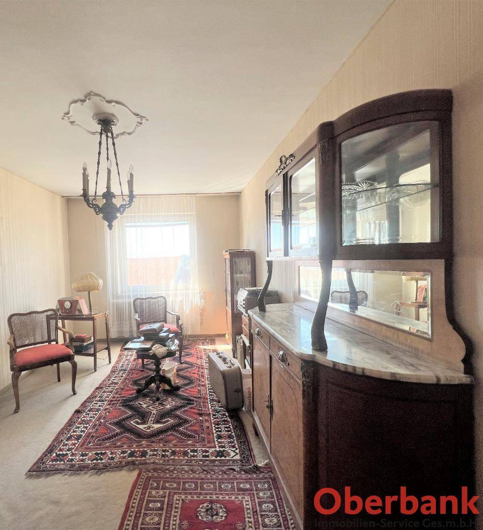 Geräumiges Wohnzimmer mit antiker Vitrine, Teppich und einem Fenster, das viel Licht hereinlässt.