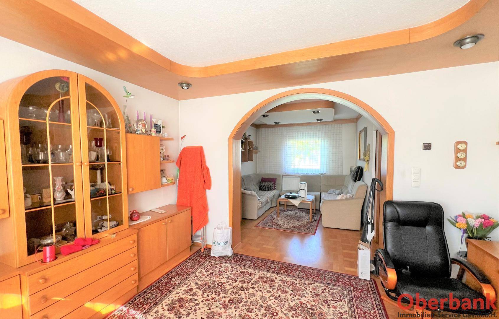 Gemütlicher Wohnbereich mit Holzboden, Teppich und einem Rundbogen zu einem weiteren Zimmer.