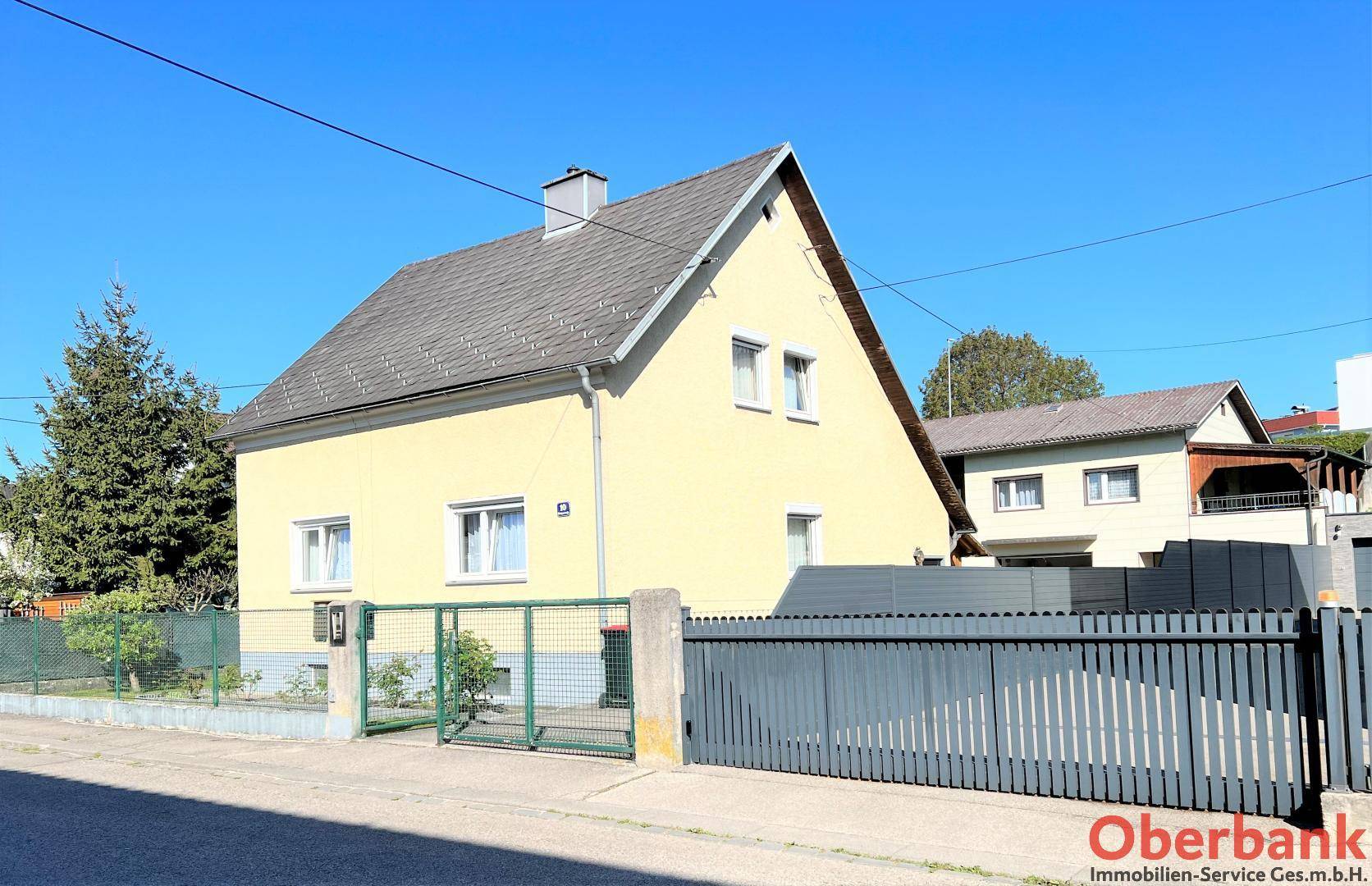 Ansicht des Hauses von der Straße mit Zaun, Einfahrt und Vorgarten.