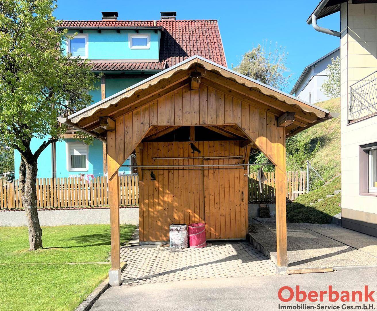 Rustikaler Holzcarport mit Satteldach und gepflastertem Stellplatz.