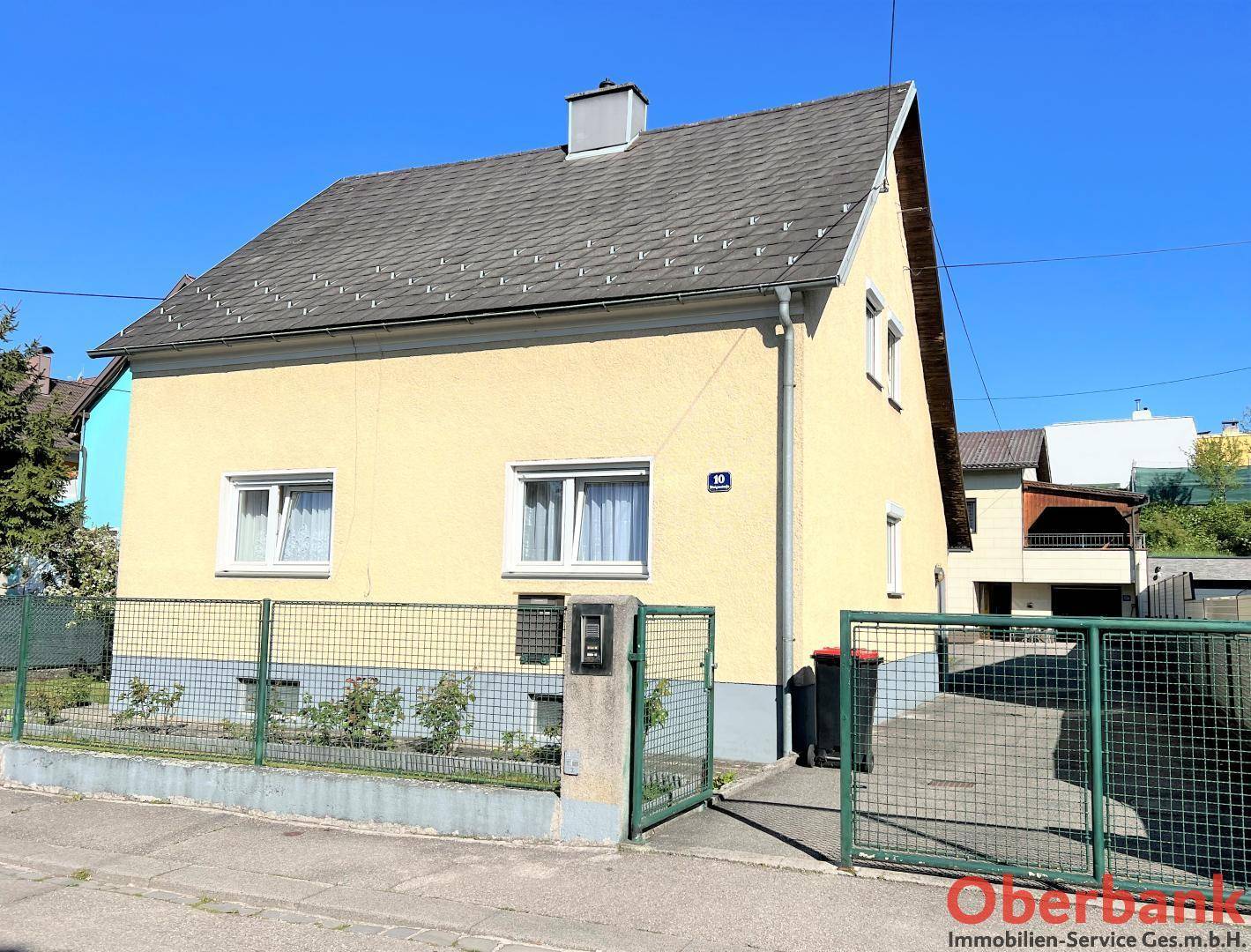 Vorderansicht des Hauses mit Zaun, Tor und gepflegtem Vorgartenbereich.