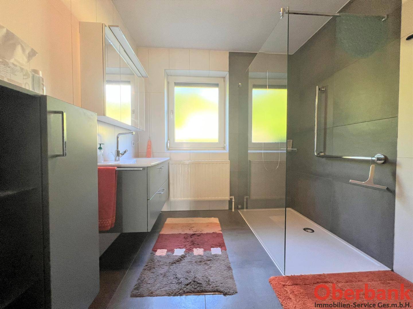 Modernes Badezimmer mit ebenerdiger Dusche, Einzelwaschbecken und zwei Fenstern.