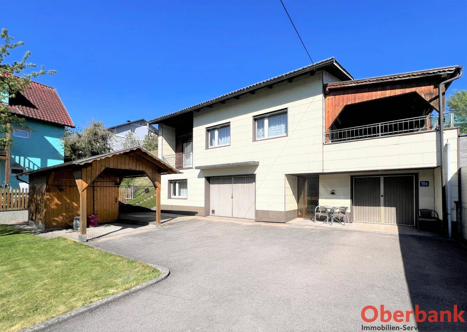 Vorderansicht des Hauses mit Garagen, Carport und Zufahrt unter blauem Himmel.