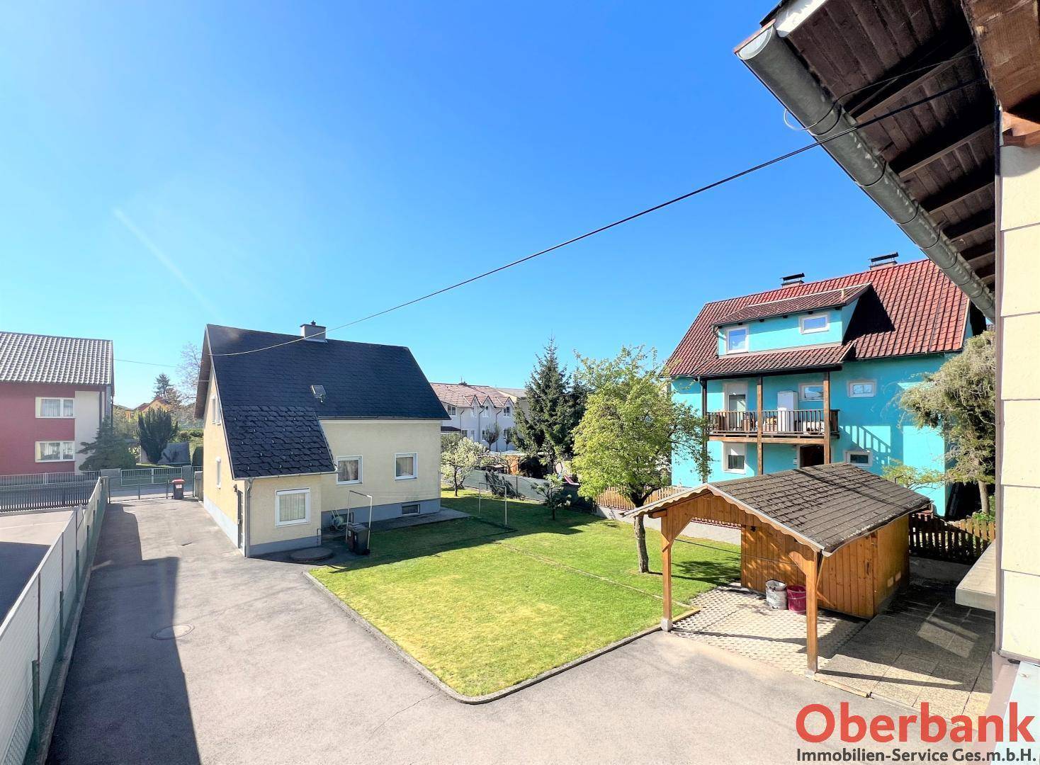 Überblick über das Anwesen mit Garten, Zufahrt und angrenzenden Gebäuden unter blauem Himmel.