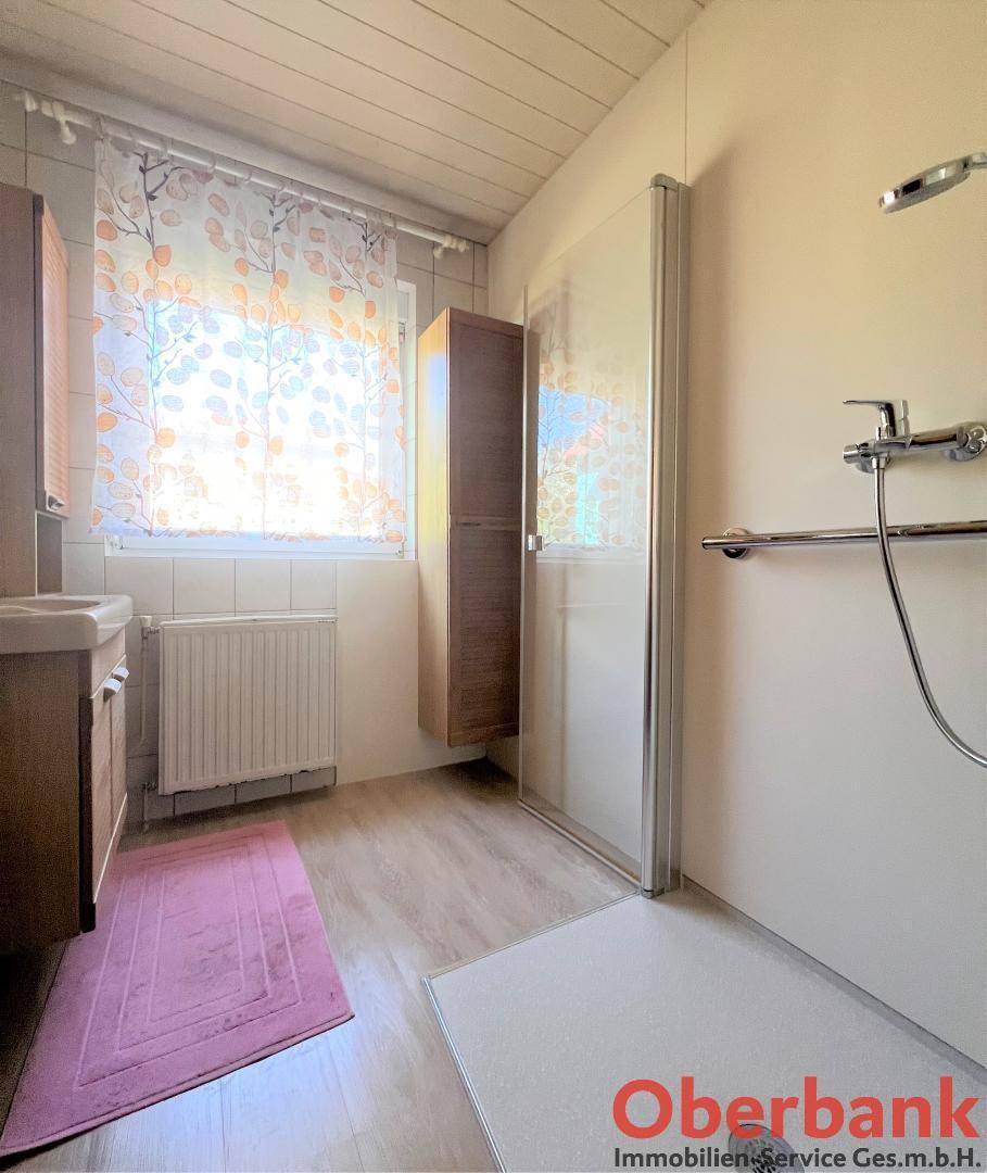 Badezimmer mit Dusche, Einzelwaschbecken, Fenster und schrägen Decken.