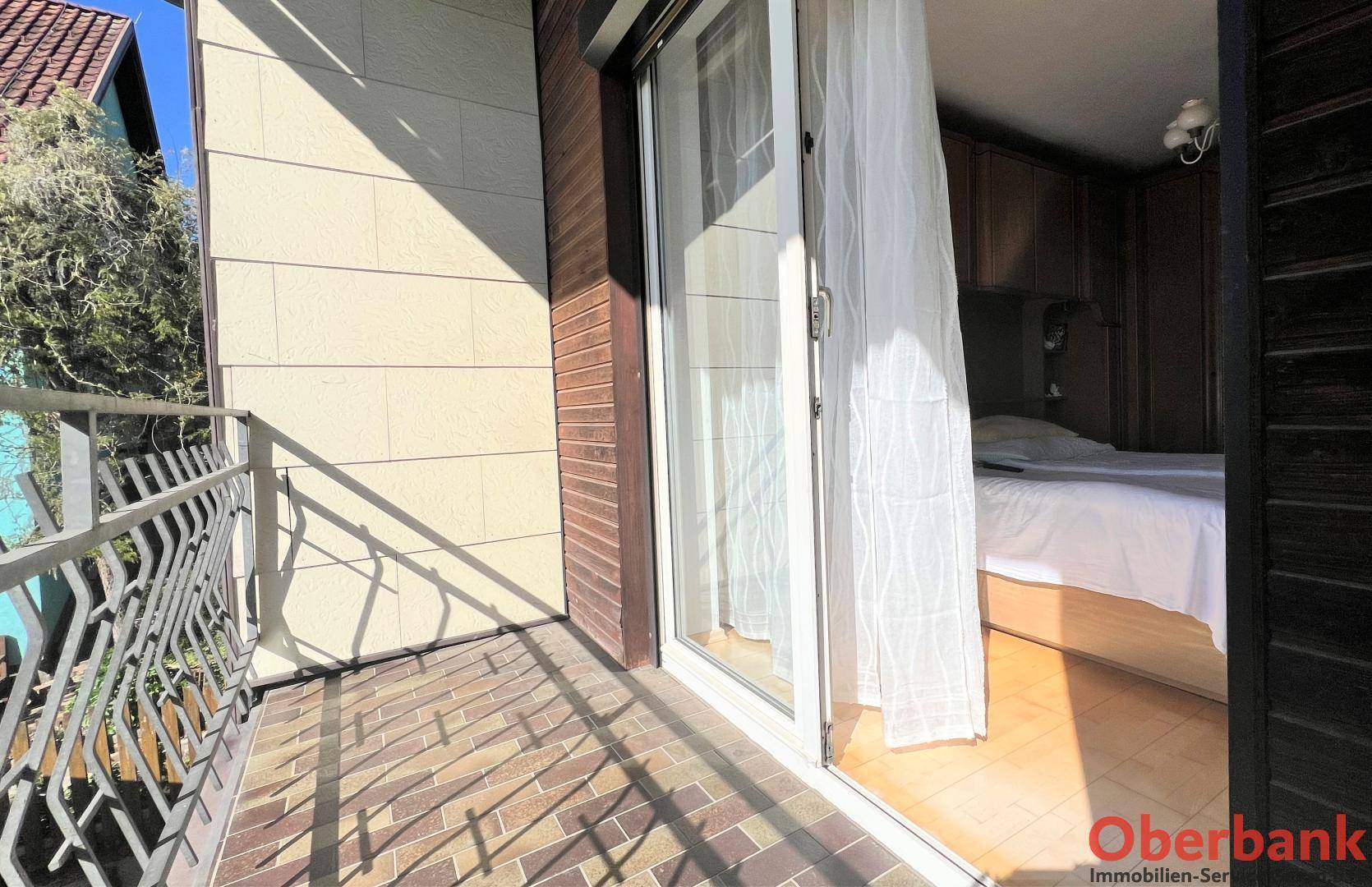 Balkon mit Fliesenboden und Zugang zu einem Schlafzimmer, umgeben von einer Brüstung.