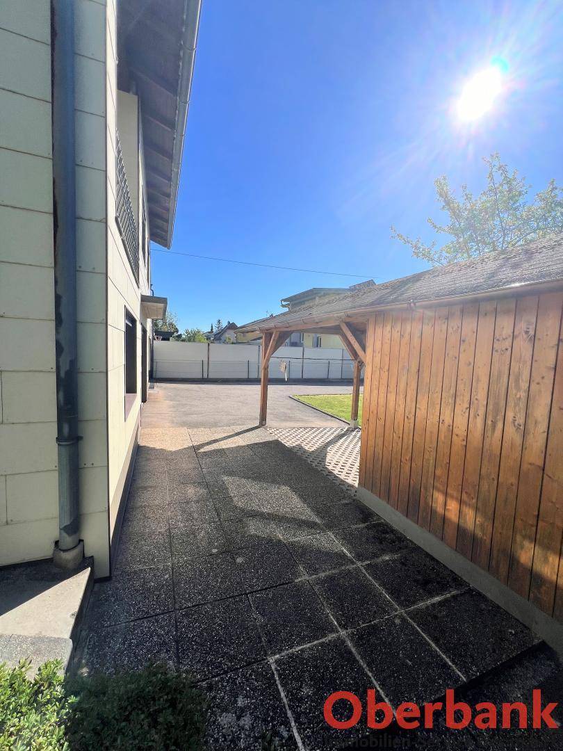 Gepflasterter Weg neben dem Haus, der zu einem überdachten Carport führt.