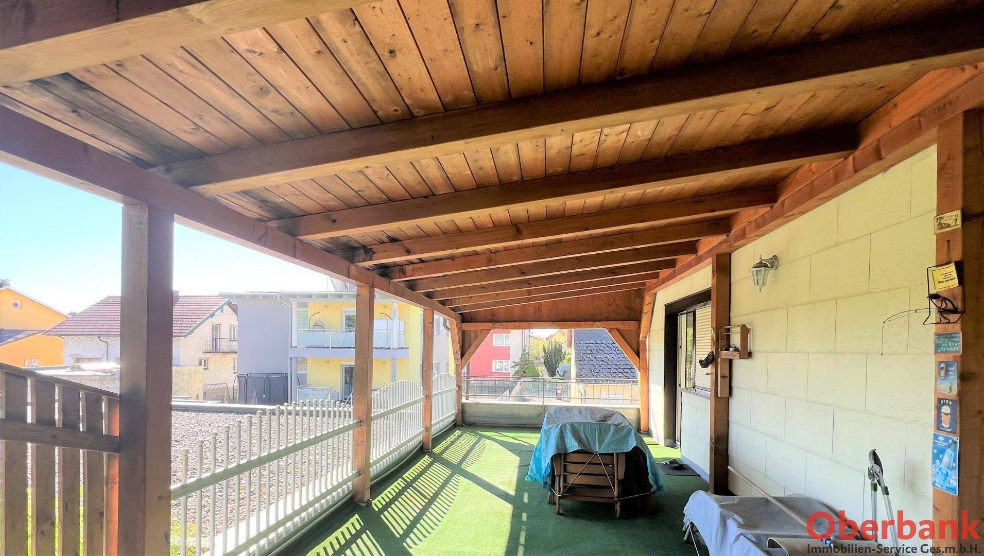 Überdachte Loggia mit Holzbalkendecke und Blick auf die Nachbarschaft.