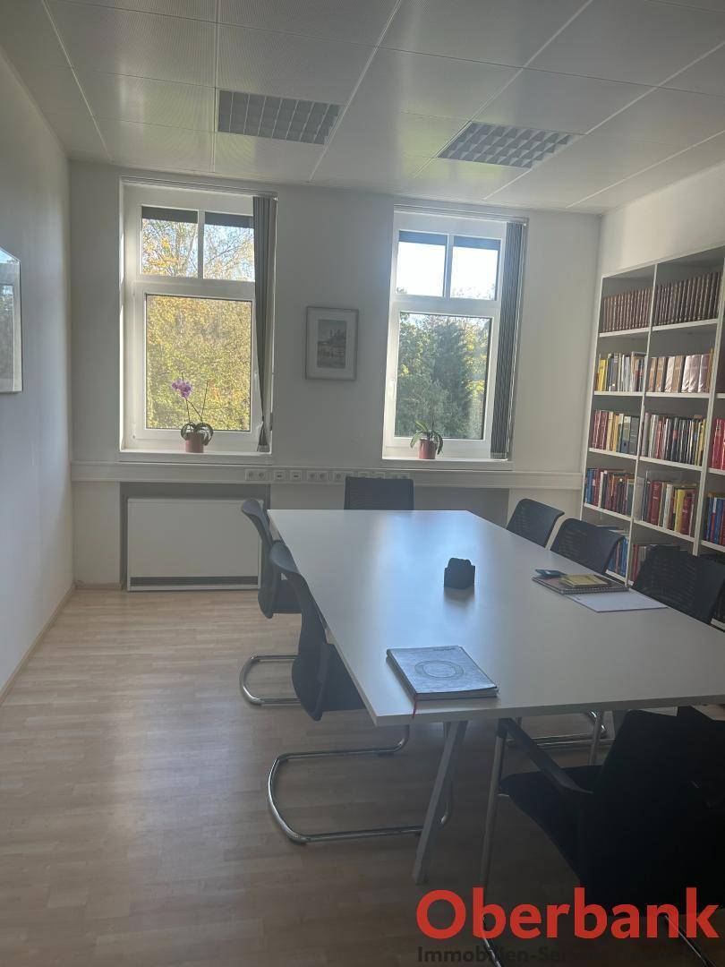 Konferenzraum mit großem Tisch, Stühlen und Bücherregal, bietet Platz für Besprechungen.