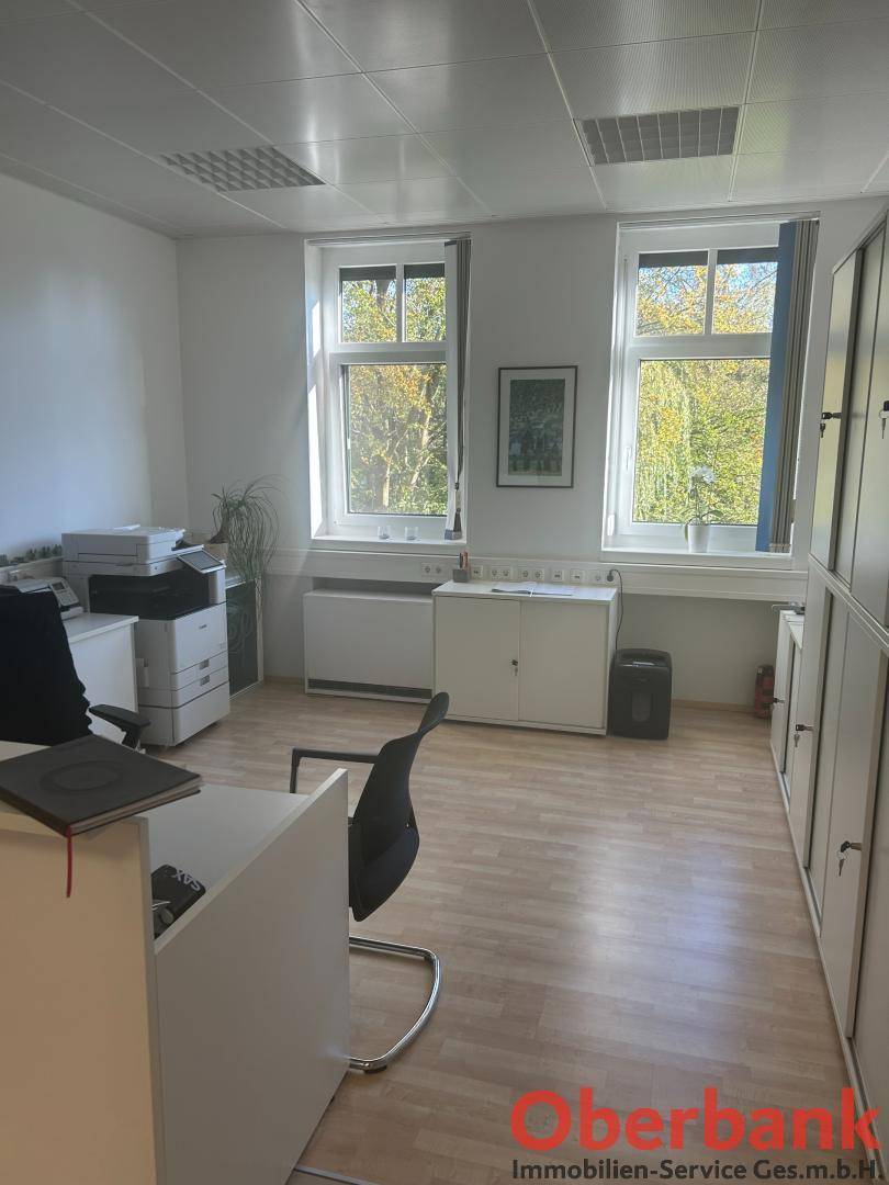 Helles Büro mit zwei großen Fenstern, Schränken und einem Drucker, ideal für Arbeitsplätze.
