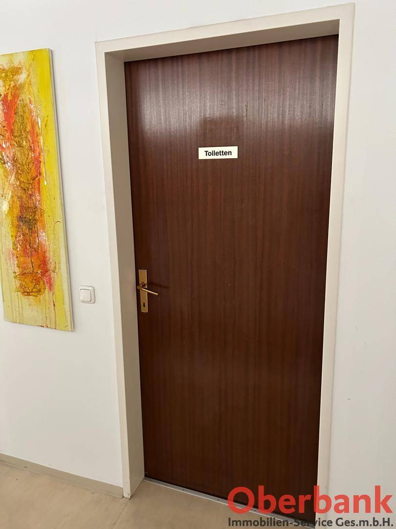 Eine braune Holztür mit einem Schild "Toiletten", die zu den Sanitäranlagen führt.