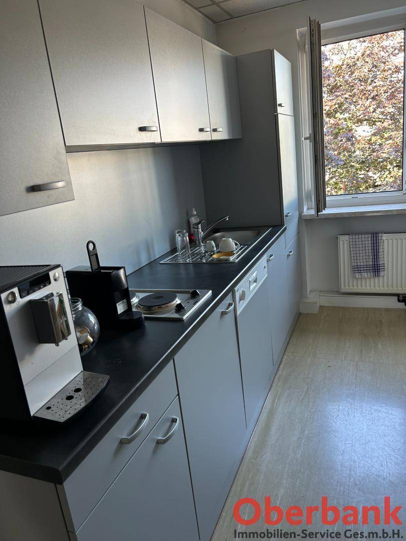 Kleine Küchenzeile mit Spüle, Kochfeld, Kaffeemaschine und grauen Schränken, ideal für Pausen.
