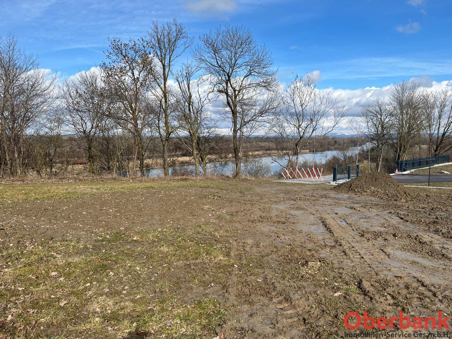 Offenes Grundstück mit Blick auf einen Fluss oder See und umliegende Bäume unter blauem Himmel.